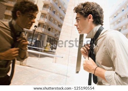 Young aspirational businessman doing up his tie knot in a golden mirror modern office building in the city.