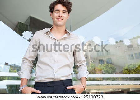 Graphic portrait of a confident businessman standing with his hands in his pockets by a modern building window with reflections of the city behind him, smiling.