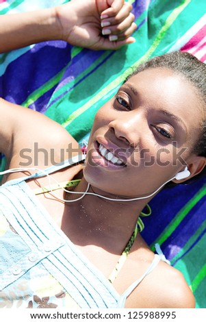 Over head portrait of an attractive african american woman listening to music while relaxing on a beach towel during her vacations.