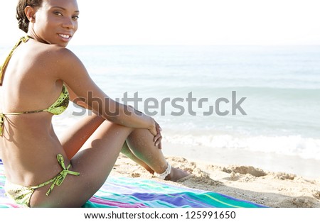 Side view of an attractive african american woman on vacation sitting on a towel on a golden beach, contemplating the sea while on vacation, smiling.