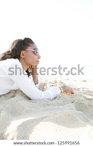 Profile view of an attractive young african american black woman contemplating the ocean while relaxing on a white sand beach on vacations.