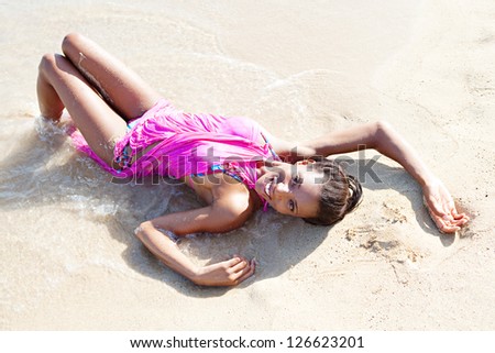 Over head beauty portrait of a black woman relaxing on a beach shore, bathing in the waves on golden fine sand, smiling at the camera.
