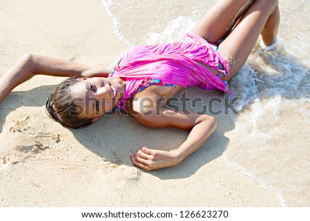 Over head beauty portrait of a black woman relaxing on a beach shore, bathing in the waves on golden fine sand, smiling at the camera.