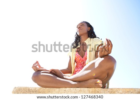 Low side view of a healthy and attractive african american woman in a yoga position meditating against a bright blue sky on a sunny day.