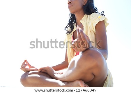 Low side body section of an african american woman in a yoga position meditating against a bright blue sky on a sunny day.
