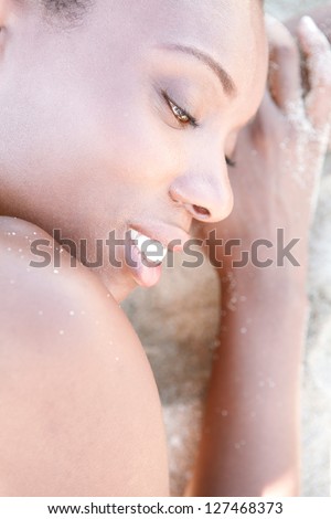 Profile close up beauty portrait of an attractive black woman with perfect skin, laying down on a white sand beach, relaxing.