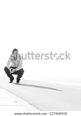 Black and white view of a sports man crouching down on a running track by the sea on a sunny day, being thoughtful.