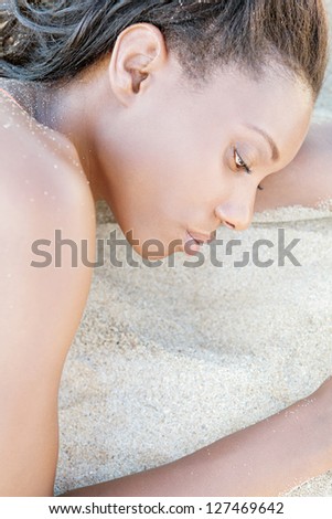 Profile close up beauty portrait of an attractive black woman with perfect skin, laying down on a white sand beach, relaxing.