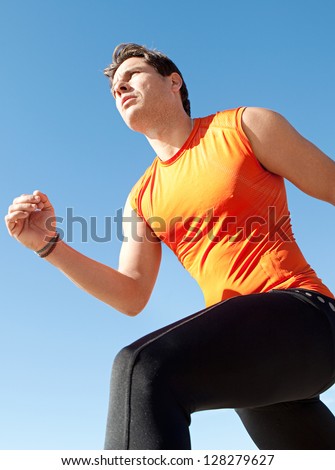 Lower perspective view of a professional olympic sports man running against a bright blue clean sky.