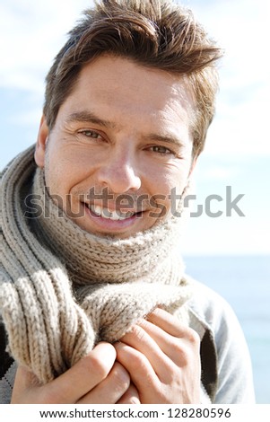 Attractive middle age man wearing a wool scarf on a sunny winter day on a beach with a blue sky.