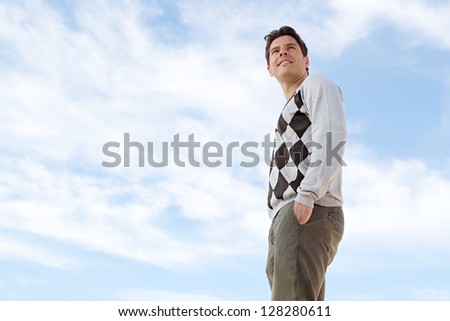 Low perspective of a smart man standing with his hands in his pockets against a deep blue sky, turning his head and smiling.