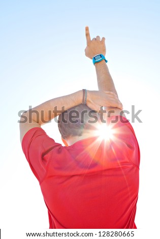 Rear view of a sports man wearing a red shirt and holding one arm up against a deep blue sky with sun rays filtering through his neck.