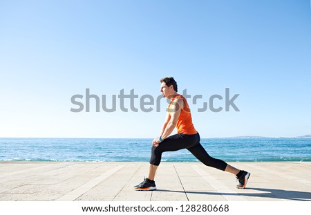 Wide profile view of a sports man figure stretching his legs on a track along the sea with the blue sky in the background and space around him.