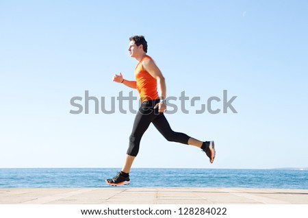 Wide profile view of a sports man running figure on a track along the sea with the blue sky in the background and space around him.