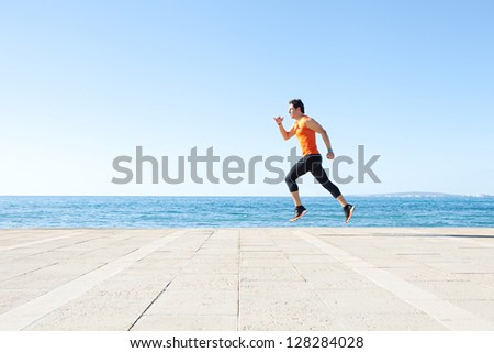 Wide profile view of a sports man running figure on a track along the sea with the blue sky in the background and space around him.