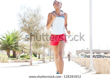 Attractive african-american woman running and exercising in the city, listening to music with her ear phones on a sunny day.