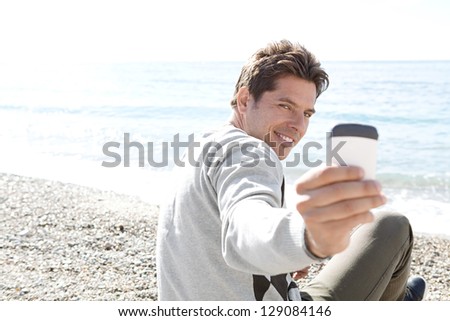 Smart man sitting down on a pebble beach, turning around to take a picture with his \