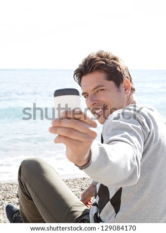 Portrait of a smart man sitting on a pebble beach, turning around to take a picture with his \