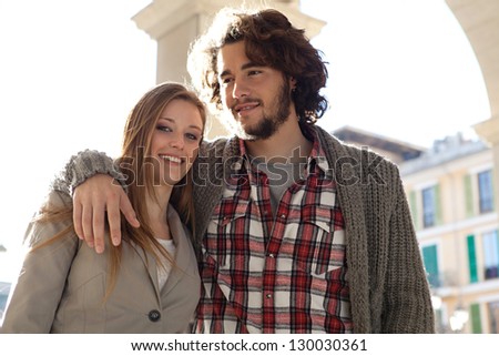 Attractive young tourist couple with arms around each other while visiting a destination city on vacation during a sunny morning.