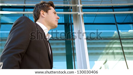 Panoramic side view of an elegant and powerful businessman in the financial city district with a modern structure office building in the background.