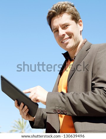 Side portrait of a businessman using a digital tablet device while standing against a deep blue sky, smiling.