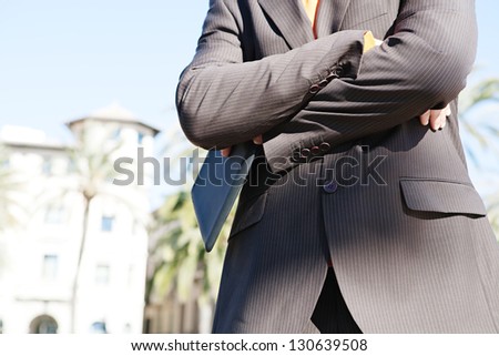 Close up view of a businessman middle body section wearing a suit and holding a digital tablet pad against a blue sky in a classic city.