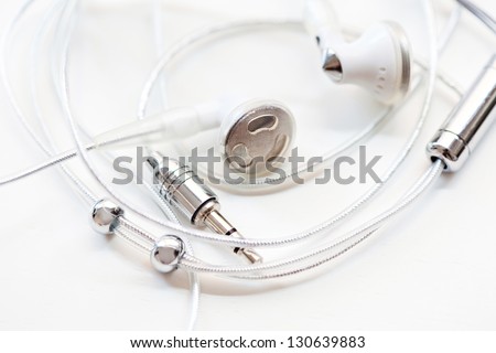 Close up detail view of a pair of musical earphones laying together with cable around them, isolated on a white background.