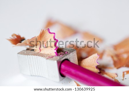 Close up view of a pink pencil being sharpened in a metallic pencil sharpener with wood shavings around it on a desk.