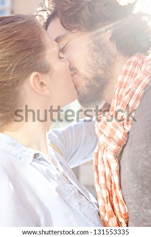 Close up view of a young attractive bohemian couple kissing outdoors with the sun rays filtering through during a sunny day.