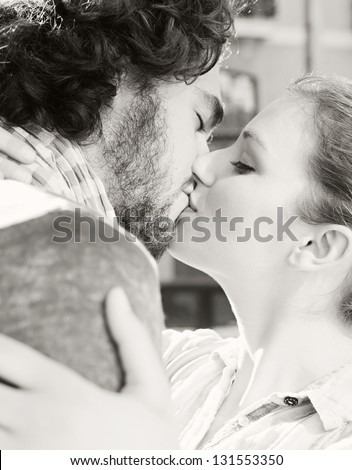 Black and white portrait profile view of an attractive young tourist couple hugging and kissing while on vacation during a sunny day.