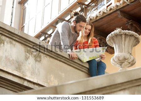 Attractive young tourist couple sitting on top of an old city stairs looking at an open street map while on holiday.