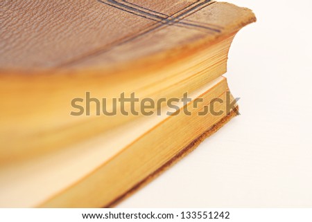 Old leather bound book being opened with gold page trims on a white desk.