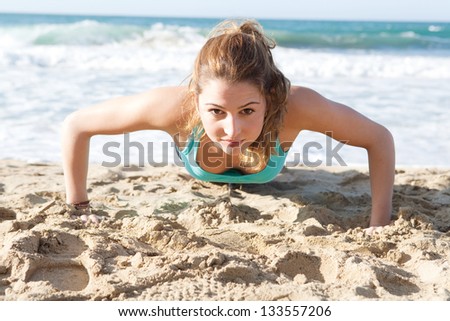 Over head view of an attractive young woman doing push ups exercises on the beach, keeping fit during a sunny day.