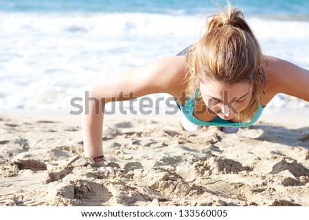 Over head view of an attractive young woman doing push ups exercises on the beach, keeping fit during a sunny day.