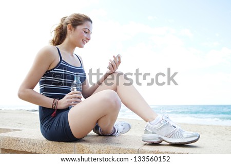 Side portrait view of a young attractive woman having a break from exercising and holding a bottle of mineral water and using a \