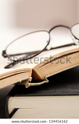 Profile view of a pair of reading glasses laying on top of some old hard back books on a desk.