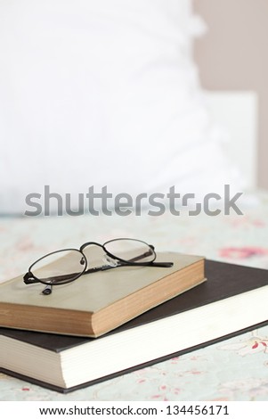 Two books and a pair of glasses laying on top of a bed in a home bedroom.