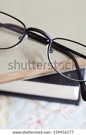 Close up detail of two books and a pair of glasses laying on top of a bed in a home bedroom.