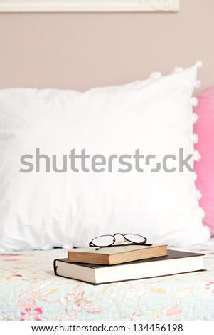 Two books and a pair of glasses laying on top of a bed in a home bedroom.