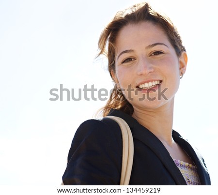 Portrait of a young professional woman wearing a black suit jacket and smiling at the camera against a sunny sky.
