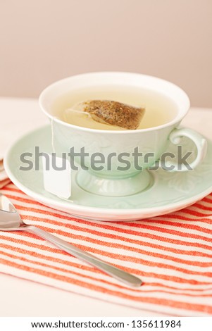Traditional cup of hot tea brewing in a decorative green porcelain cup on a red and white stripy napkin in a home kitchen.