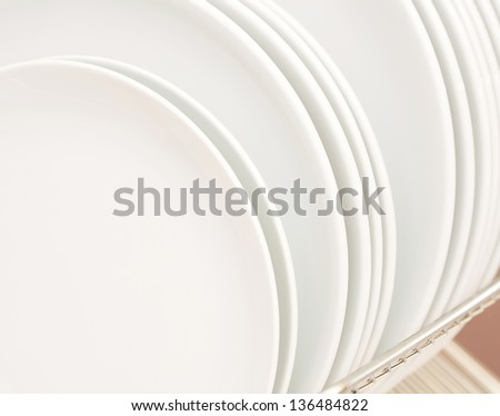 Close up detail background view of different sizes white plates and dishes on a drying rack in a kitchen table.