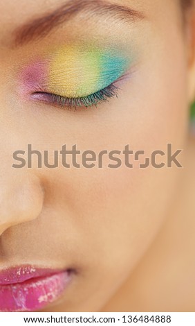 Half face portrait of a young african american girl wearing a rainbow eye shadow cosmetics and keeping her eyes closed.