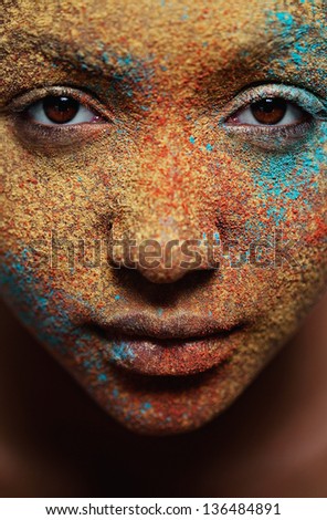 Close up portrait view of a black african american girl face with different color cosmetics powder splashes on her skin with texture and detail.