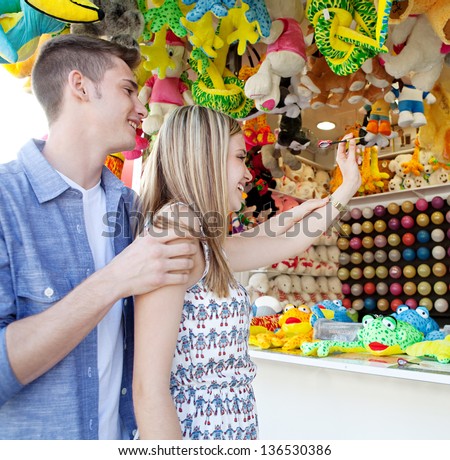 Young couple playing darts at an attractions fair ground, aiming together to win a prize, outdoors.