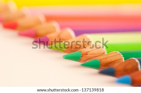 Diagonal line of differently colored drawing pencils on a white writing desk, over head close up detail view.
