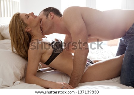 Profile view of a sexy and attractive couple being passionate and kissing in bed while wearing jeans and lingerie.