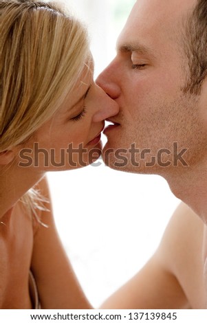 Profile close up portrait of an attractive couple kissing and being passionate in bed, with their lips touching gently.