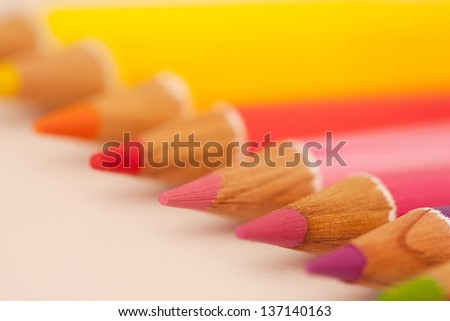 Diagonal perspective of various colored drawing pencils on a white writing desk, over head close up detail view.
