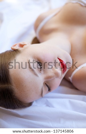 Over head beauty portrait of an attractive young woman sleeping on a white bed, wearing white lingerie and glossy red lips.